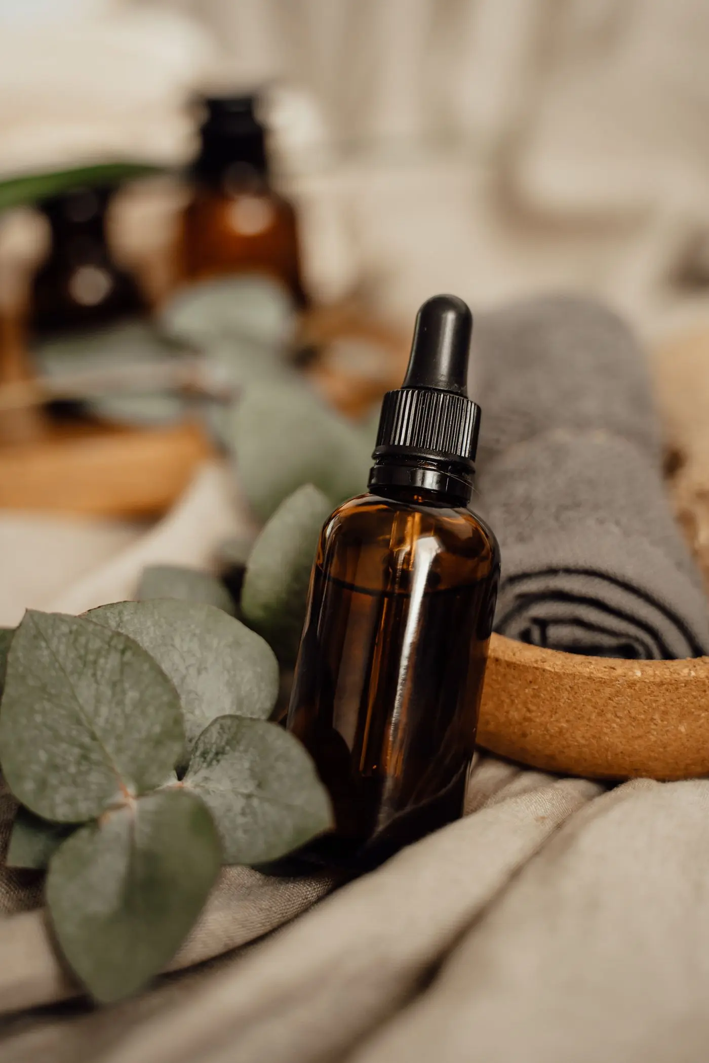 An amber dropper bottle beside towels and eucalyptus leaves