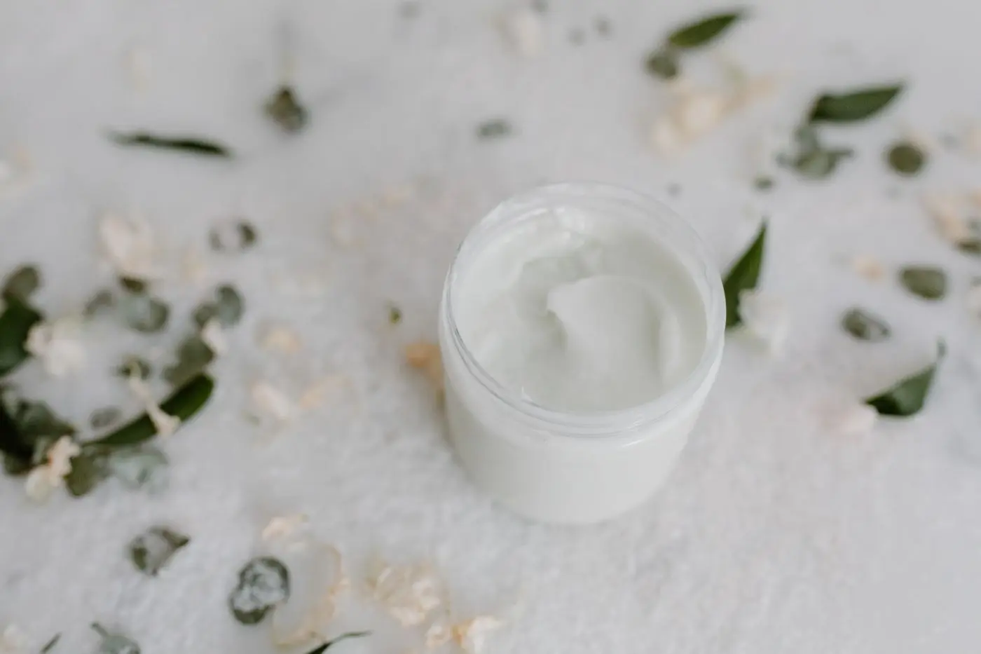 An open cream jar with botanical leaves on a light surface