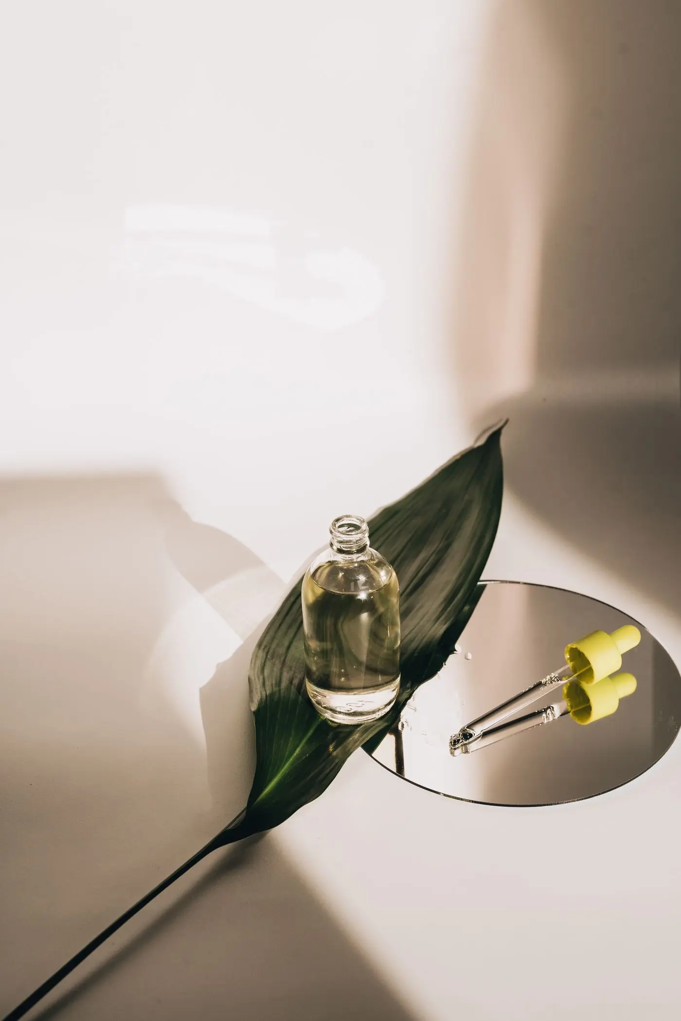 A glass serum bottle beside a green leaf in warm light